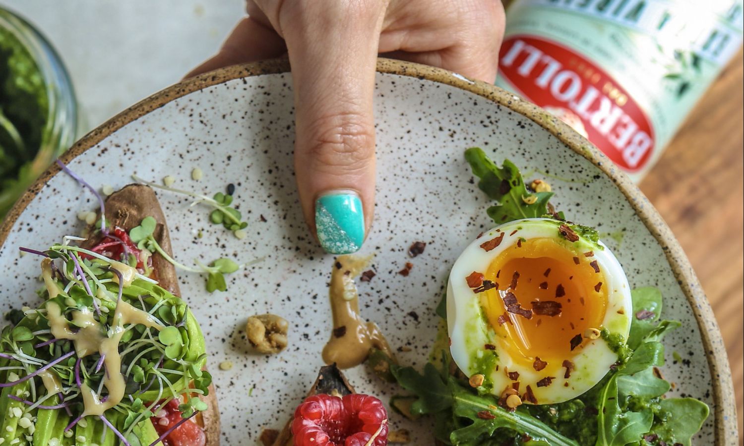 A plate with veggies and an egg on it alongside a bottle of Bertolli extra virgin olive oil. Italian cooking recipes.